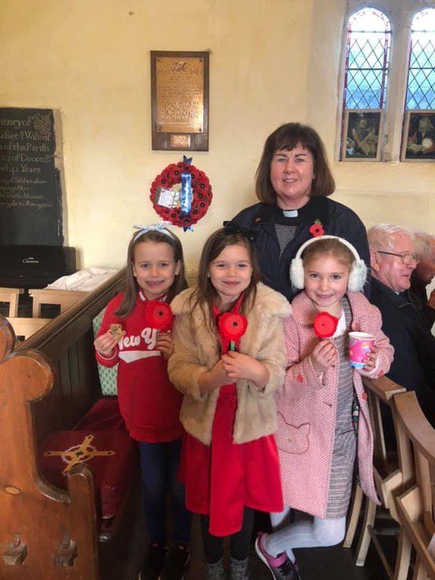 A priest with a group of schoolchildren holding poppies