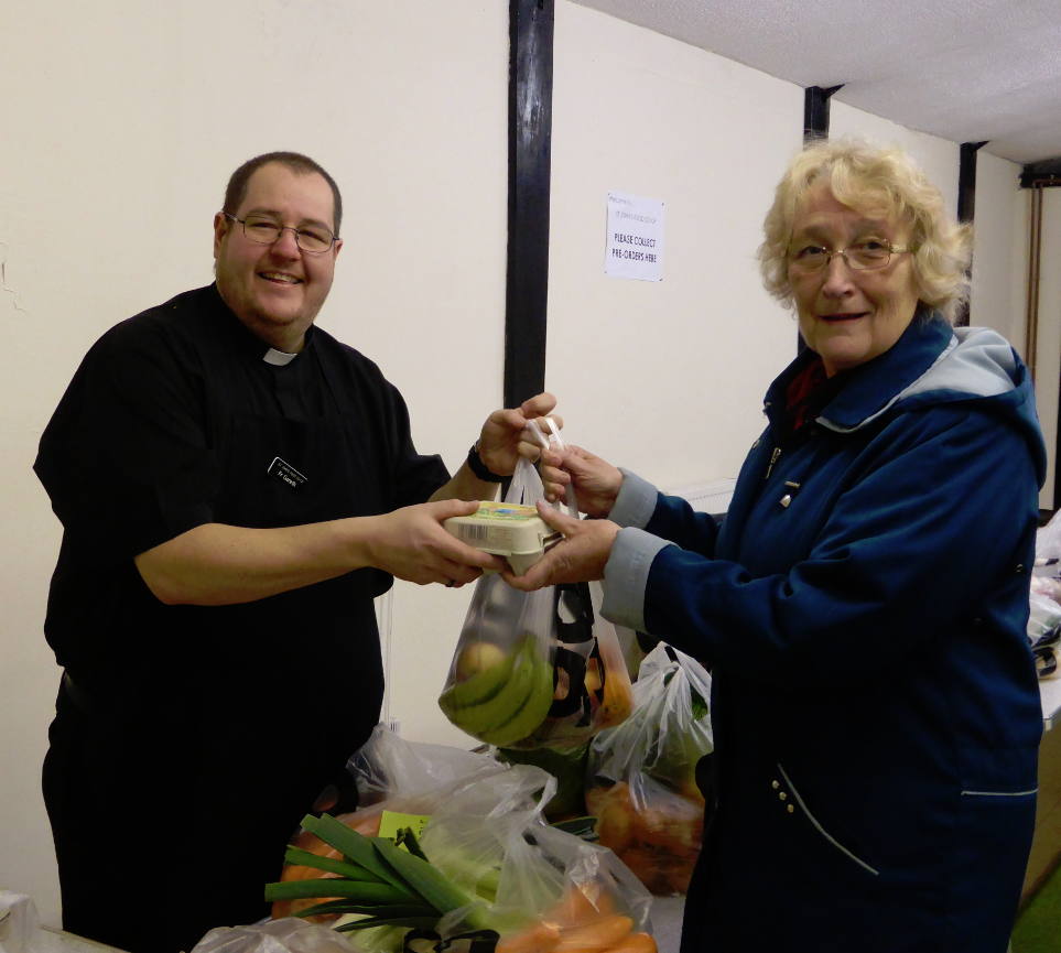 Priest giving food to woman as part of Food co-op programme