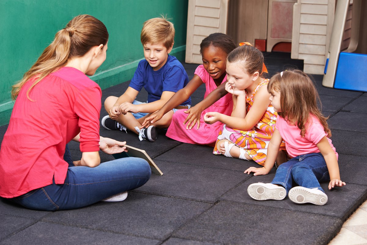 Four children sitting down and sharing a book with an adult