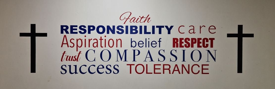 A banner on the wall at St John Baptist CinW High School detailing the school's values- faith, responsibility, care, compassion, respect, trust, success and tolerance