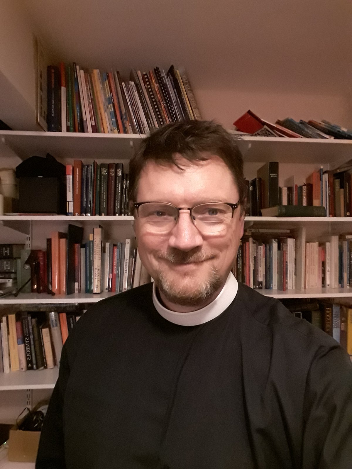 Tim Jones, smiling, wearing glasses and a cassock