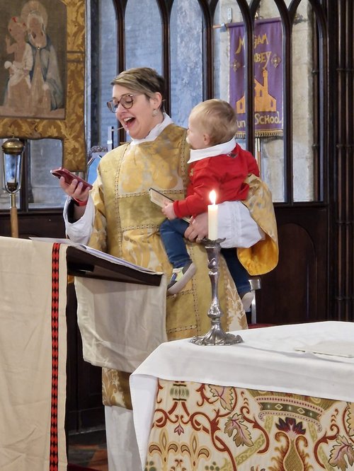 ruth holding a baby and the alter and reading a prayer from her phone